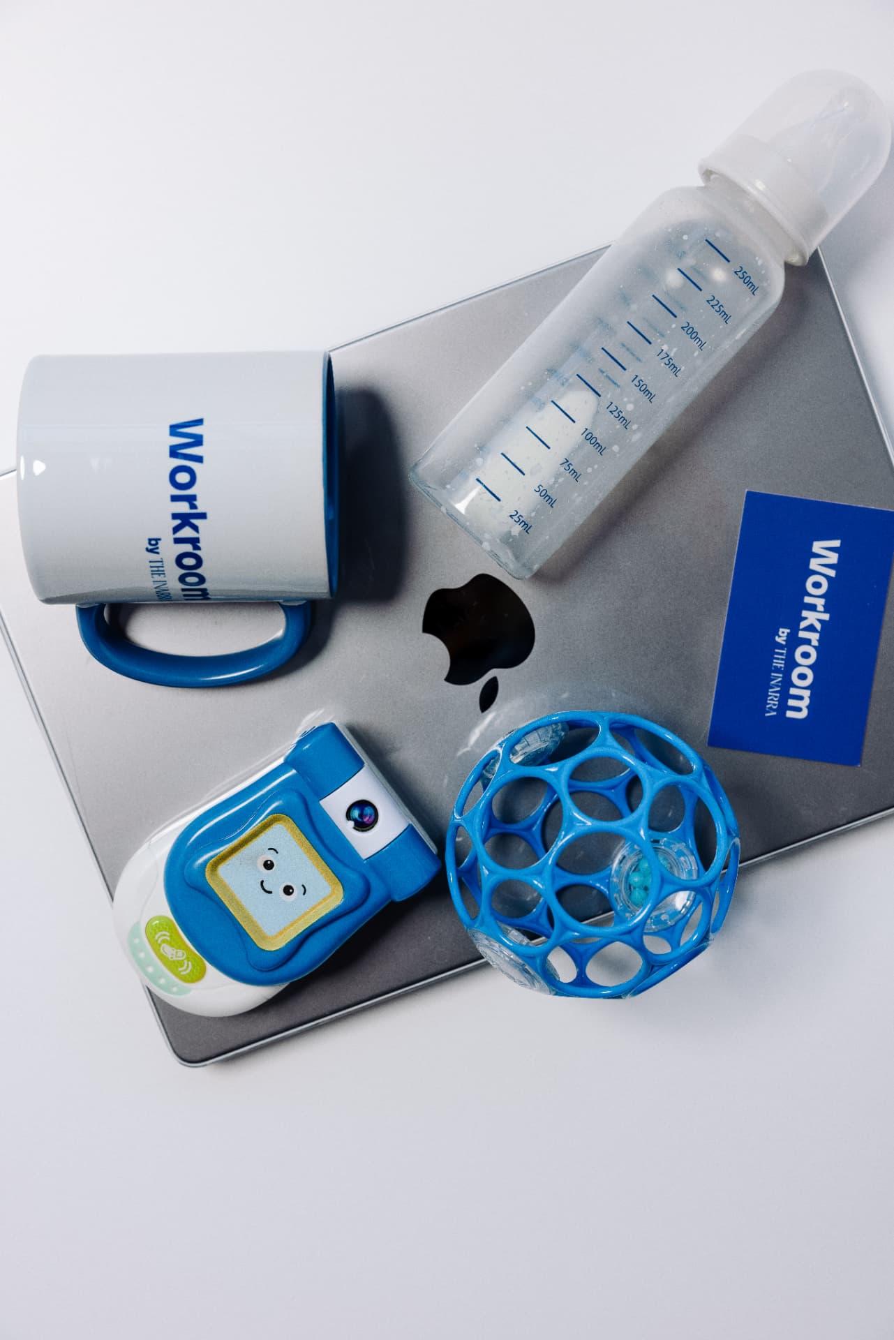 A Workroom mug, business card, baby bottle and toys on a laptop